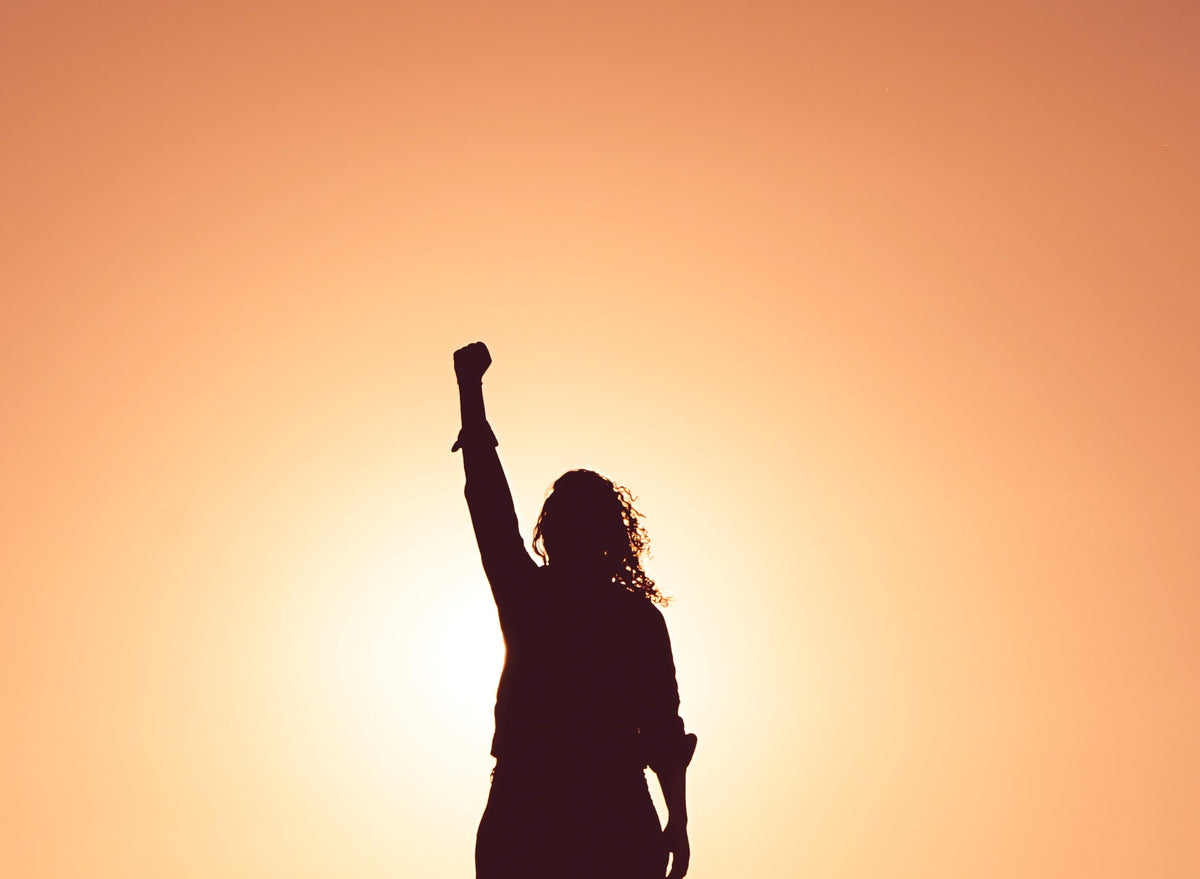 A woman holds up a fist in front of the sunset. 